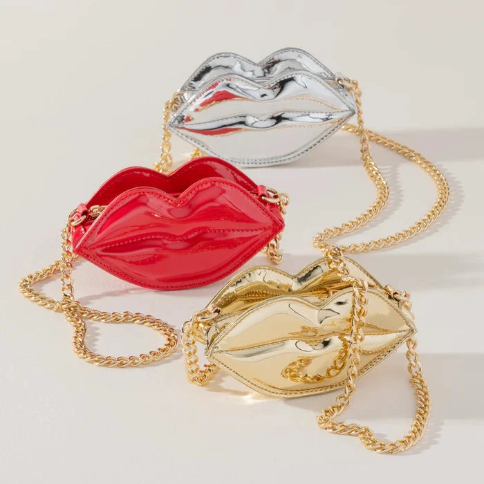 Three lip-shaped handbags in red, gold, and silver on a light background