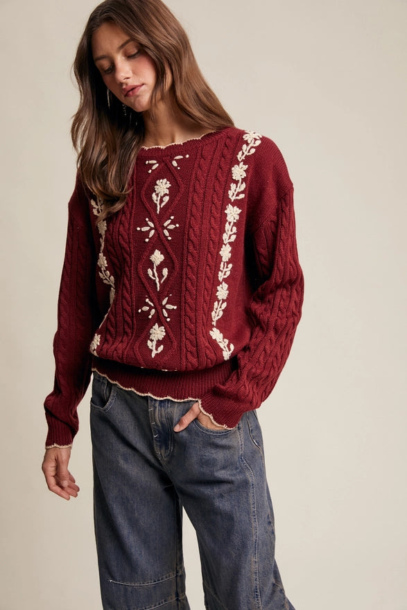 Woman wearing a burgundy sweater with white embroidery on a beige background