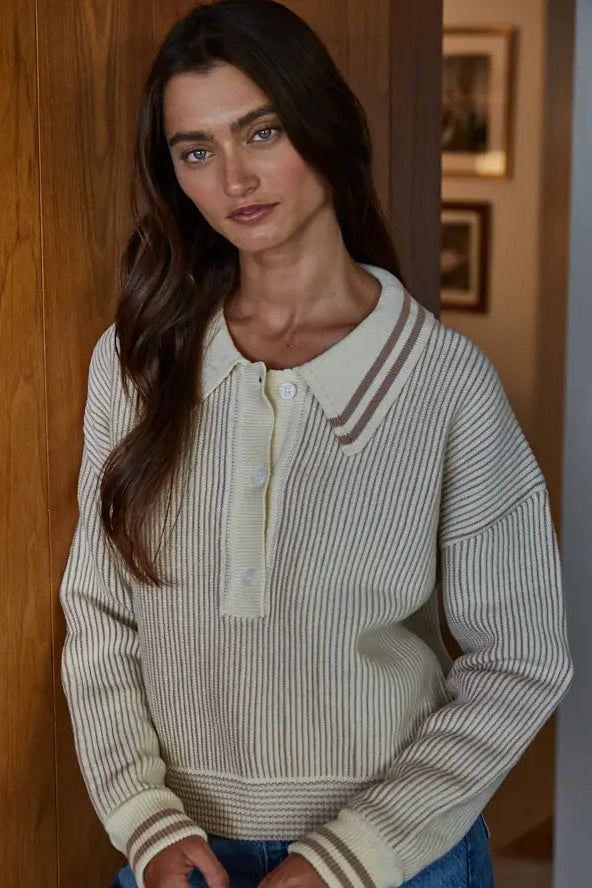 Woman wearing a striped sweater standing indoors with wooden walls.