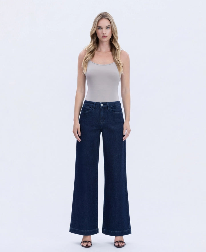 Woman wearing a white tank top and dark blue jeans on a white background