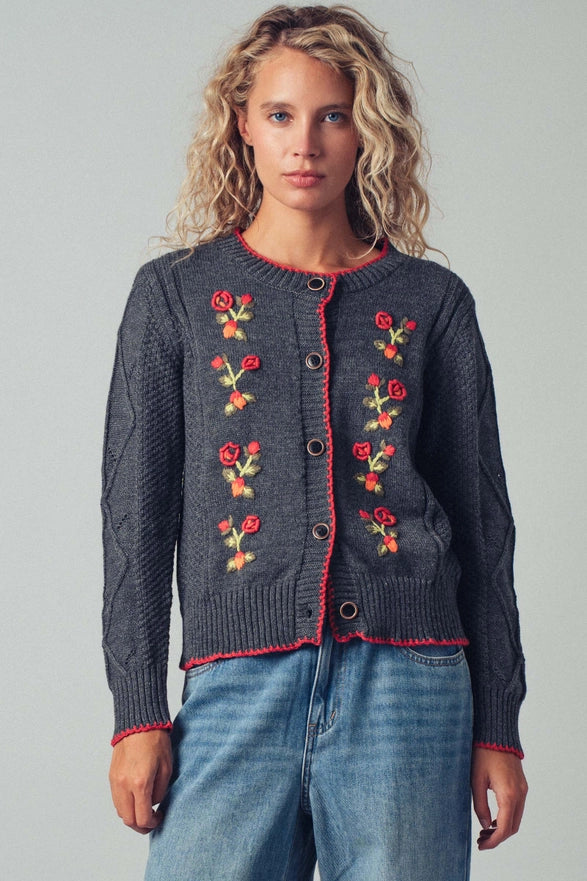 Woman wearing a dark gray cardigan with floral embroidery on a plain background
