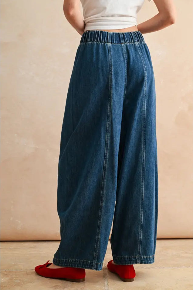 Person wearing blue wide-leg jeans and red shoes on a beige background