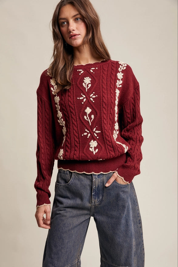 Woman wearing a red sweater with white floral patterns and blue jeans on a beige background