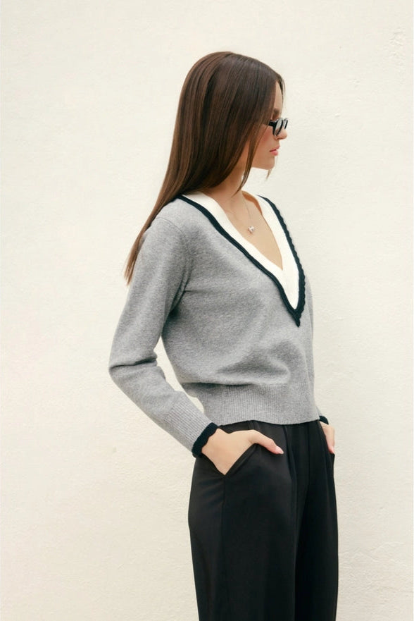 Woman wearing a gray sweater with a white collar against a beige background
