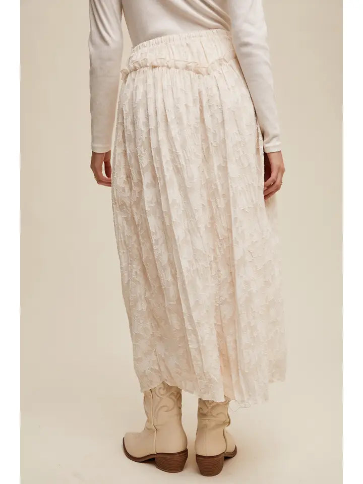 Person wearing a long beige skirt and white top on a plain background