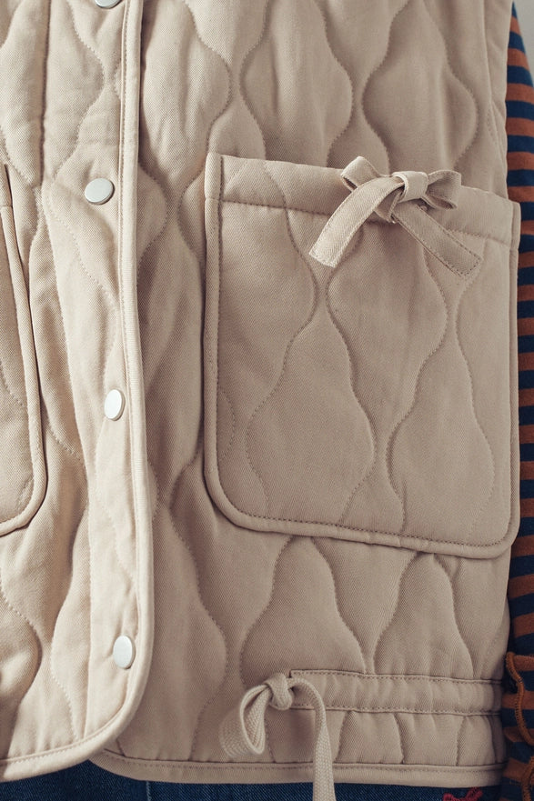 Beige quilted vest with a pocket and buttons on a striped fabric background