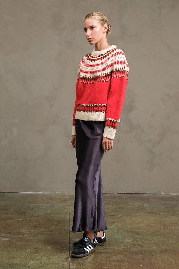 Person wearing a red and white patterned sweater with purple pants against a plain background