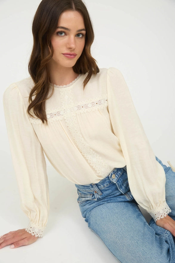 Woman wearing a cream blouse with lace details and blue jeans on a white background