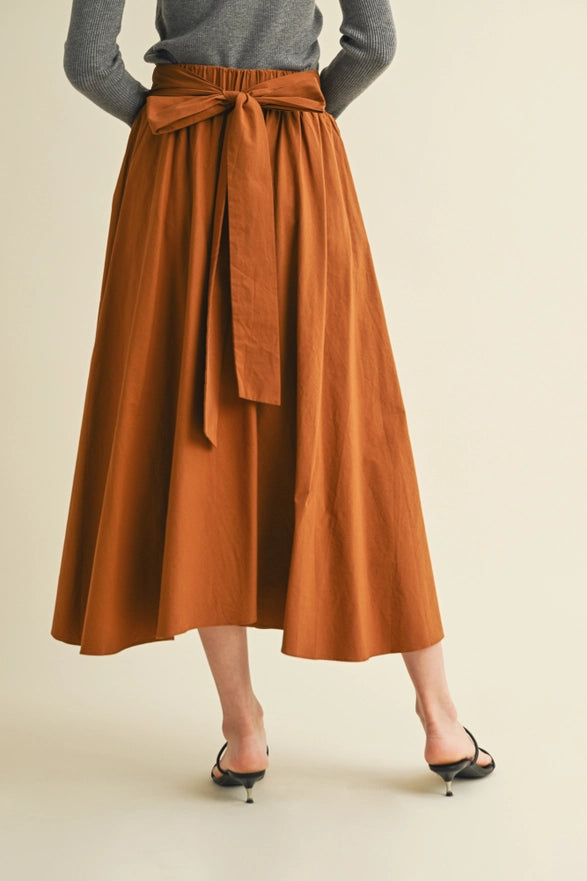 Person wearing a rust-colored skirt with a belt on a beige background
