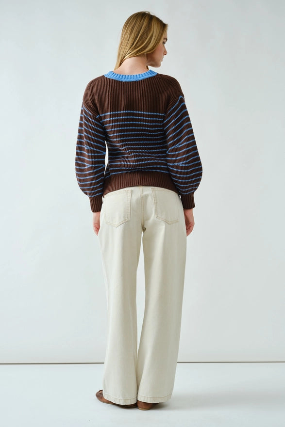 Person wearing a striped sweater and white pants against a white background