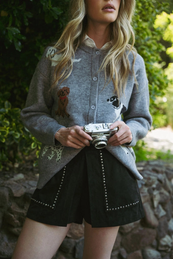 Person wearing a gray cardigan with embroidered details, holding a vintage camera, standing outdoors.