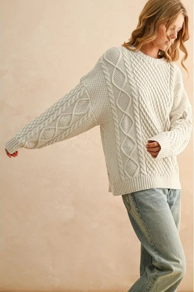 Woman wearing a white cable knit sweater and jeans against a beige background
