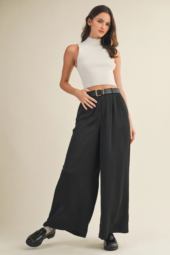 Woman wearing a white sleeveless top and black wide-leg pants on a beige background