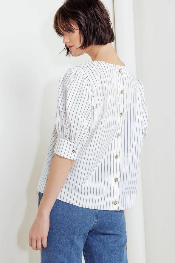 Woman wearing a white striped shirt with gold buttons and blue jeans against a white background