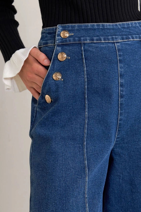 Close-up of blue jeans with gold buttons on a plain background