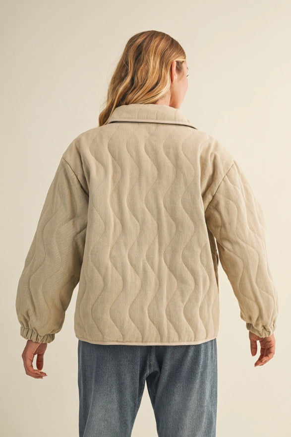 Person wearing a beige quilted jacket on a plain background
