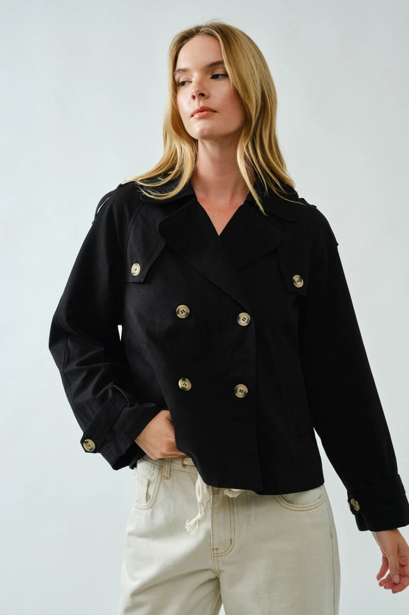 Woman wearing a black coat with gold buttons on a plain background