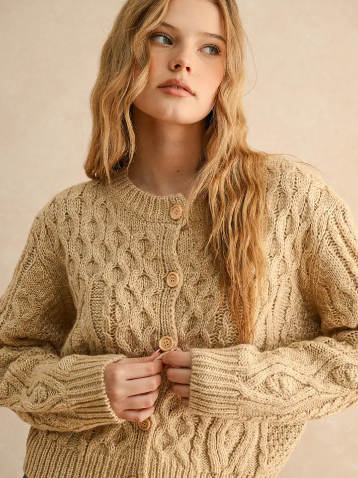 Woman wearing a beige cable knit sweater against a neutral background