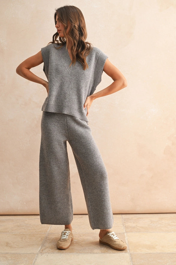 Woman wearing a gray sleeveless top and wide-leg pants against a beige wall.