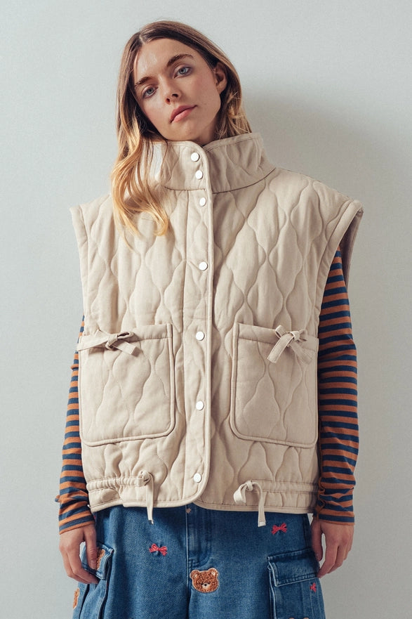 Woman wearing a beige quilted vest against a plain background