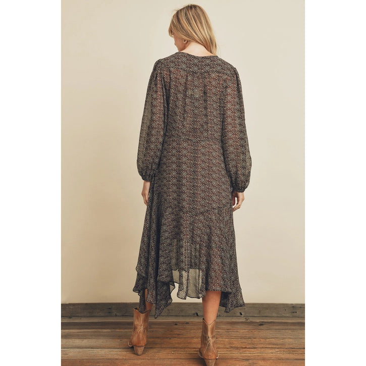 Woman wearing a long, patterned dress with brown boots against a beige wall.