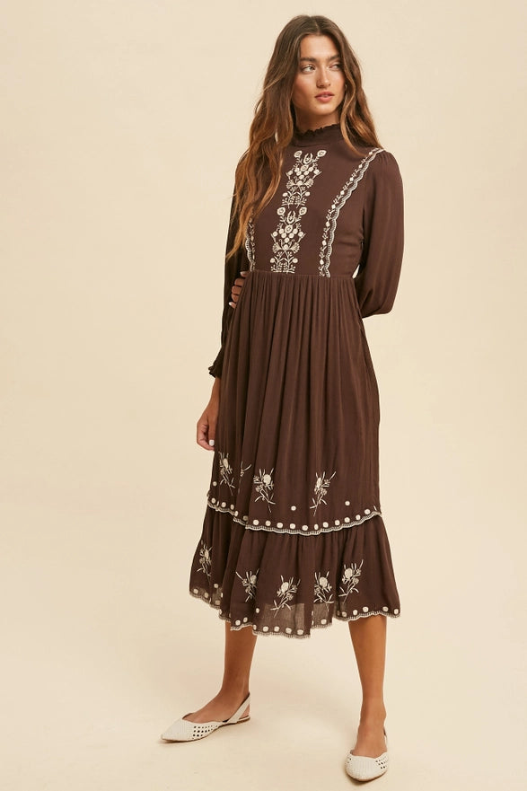 Woman wearing a brown dress with intricate white embroidery on a beige background