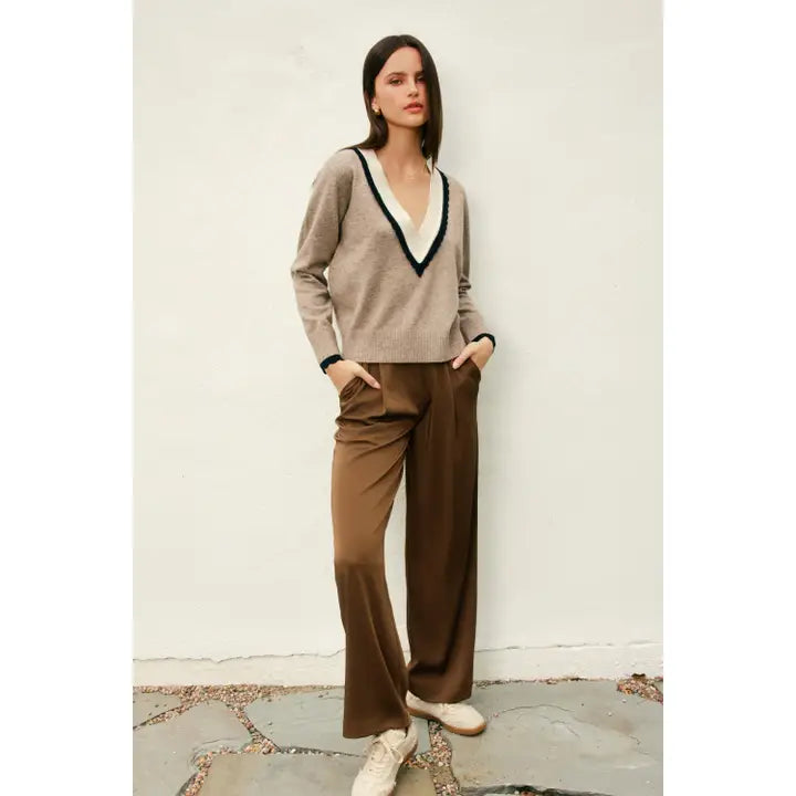 Woman wearing a beige sweater and brown pants against a plain background