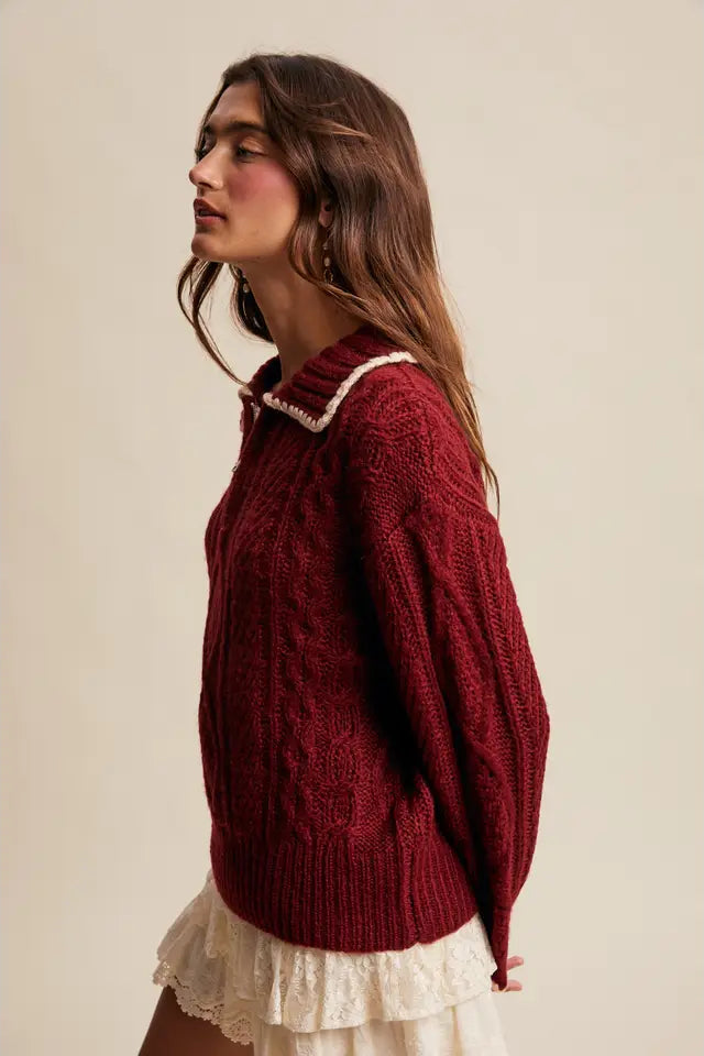 Woman wearing a red cable knit sweater with a white lace top underneath on a beige background