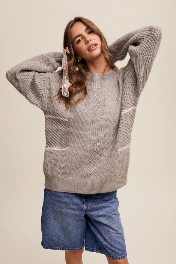 Woman standing against a plain background wearing a heather grey pull over sweater