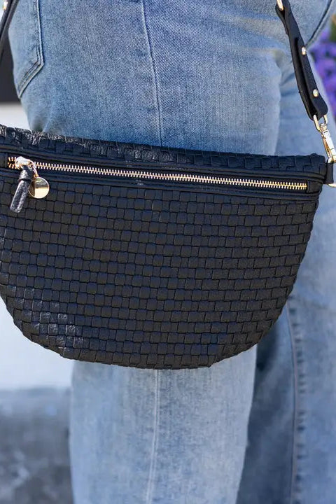 Black woven handbag with gold zipper and accents worn by a person in jeans.