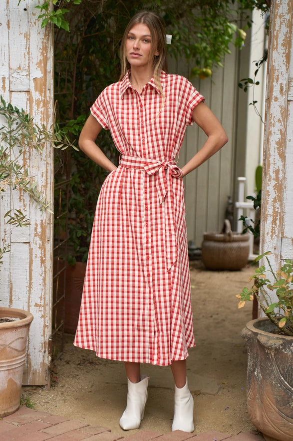 Woman wearing a red and white checkered dress standing in an outdoor setting with plants.