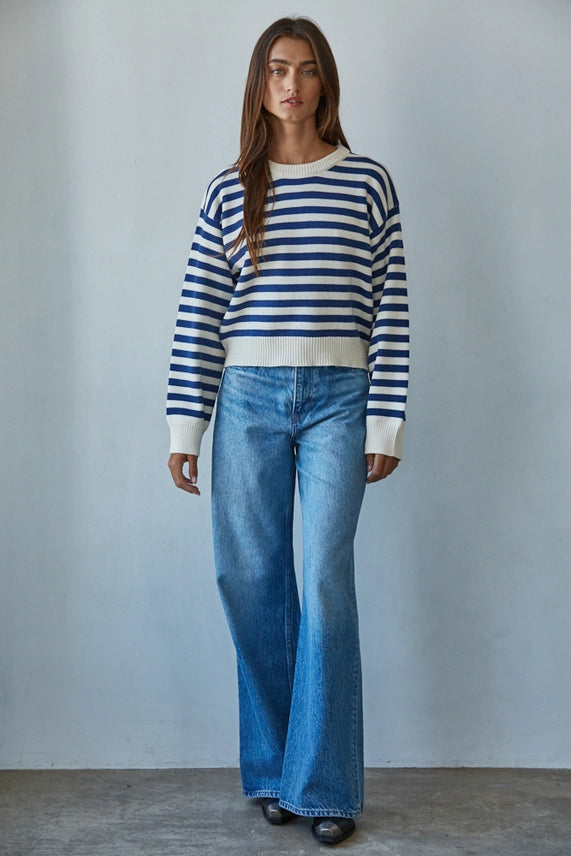 Woman wearing a blue and white striped sweater and blue jeans against a plain background