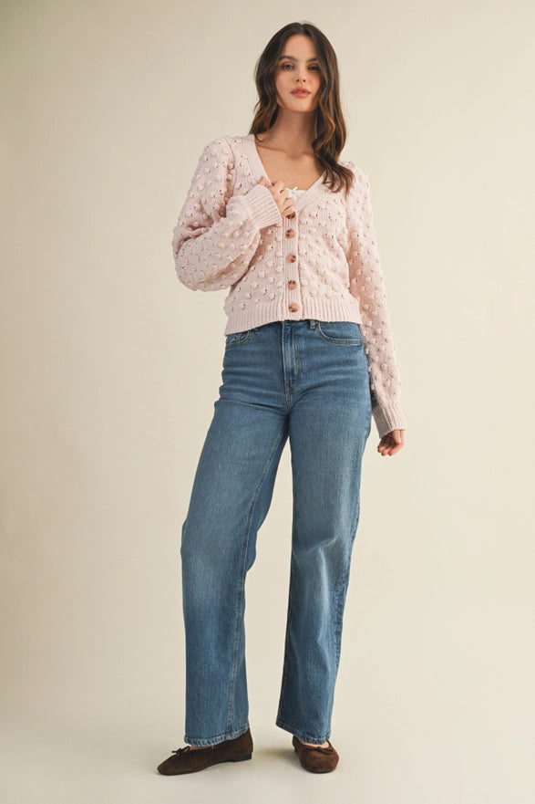 Woman wearing a light pink cardigan over a white top and blue jeans on a beige background