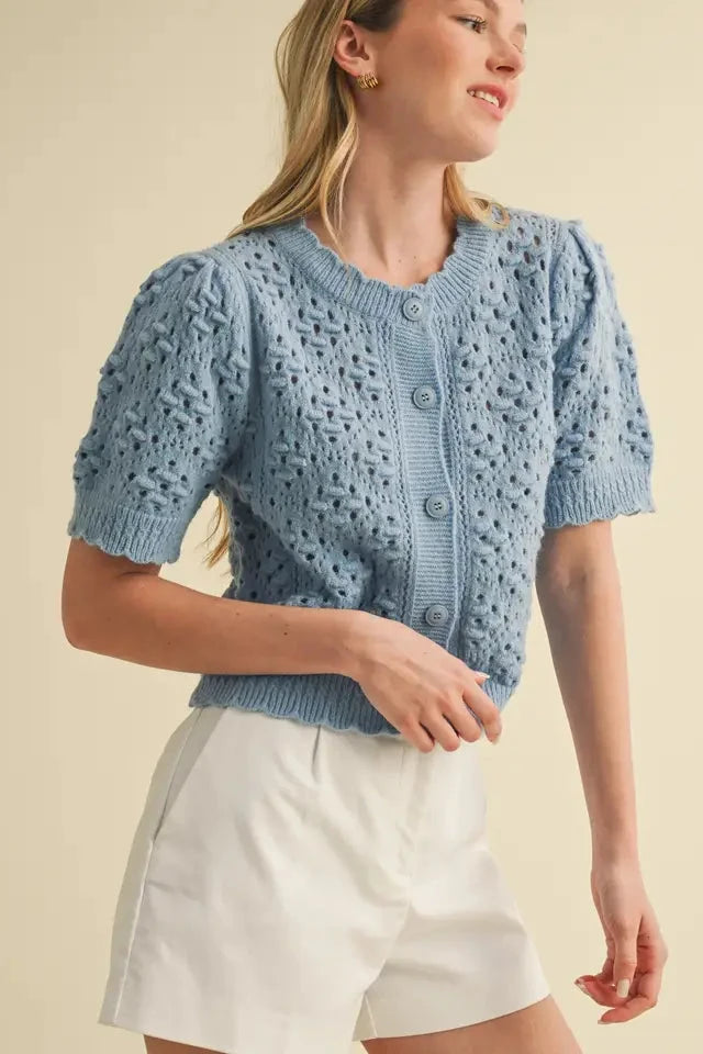 Woman wearing a light blue knitted cardigan over a white top against a beige background