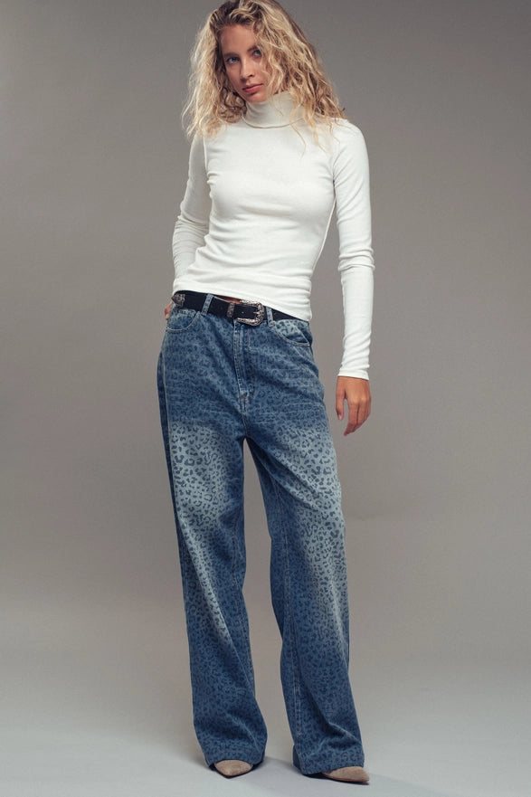 Woman wearing a white turtleneck and blue jeans against a plain background