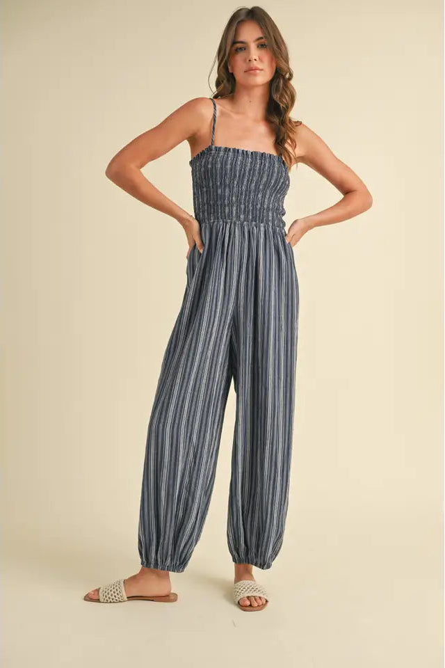 A model wearing a navy and white striped jumpsuit with spaghetti straps and a smocked bodice.