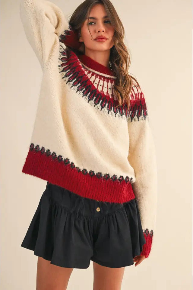 Woman wearing a cream sweater with red and black pattern, paired with a black skirt.