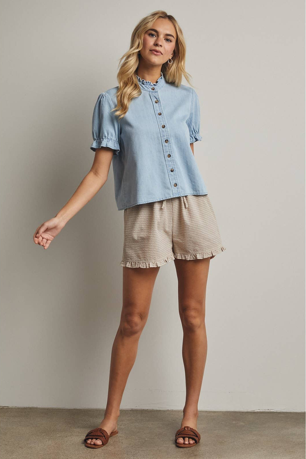 Woman wearing a light blue shirt and beige shorts against a neutral background