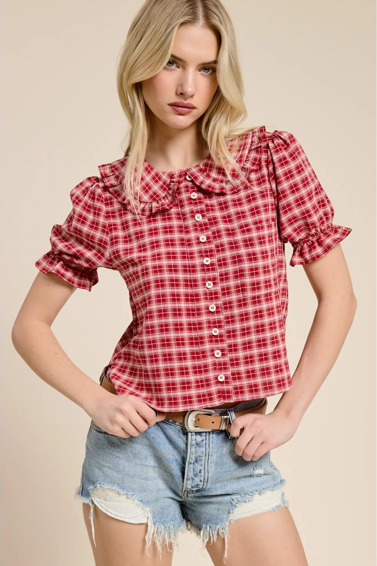 Woman wearing a red plaid shirt and denim shorts on a beige background