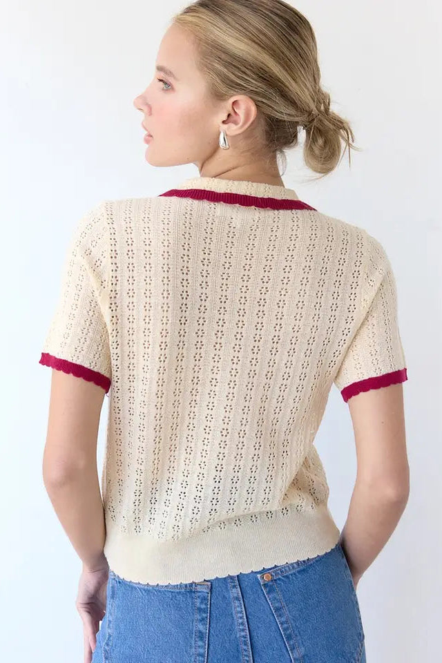 Woman wearing a beige knitted cardigan with red trim on a white background
