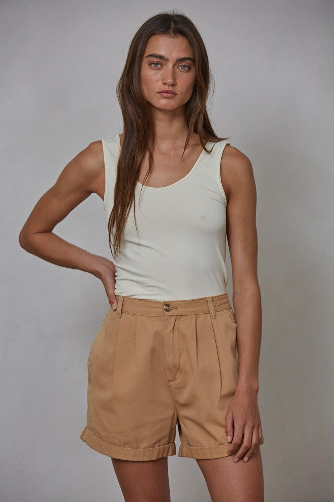 Woman wearing a light green tank top and beige shorts against a gray background