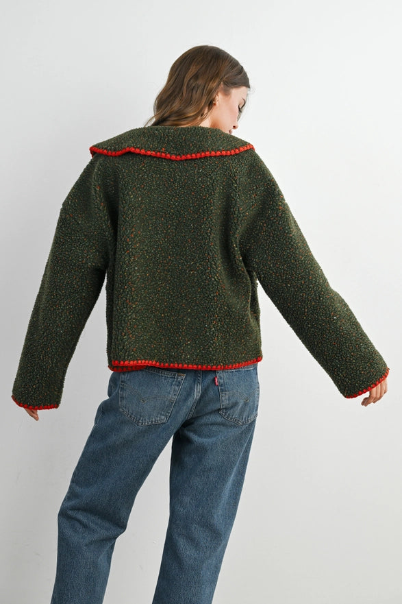 Person wearing a green knitted sweater with red trim on a white background