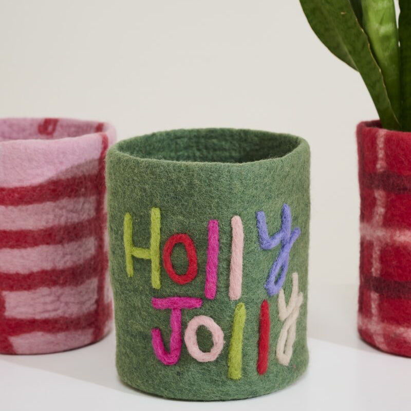 Green felt cup with 'Holly Jolly' text, surrounded by plaid fabric and a plant.