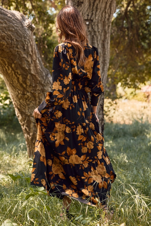 Woman in a black floral dress standing in a natural setting with trees and grass.