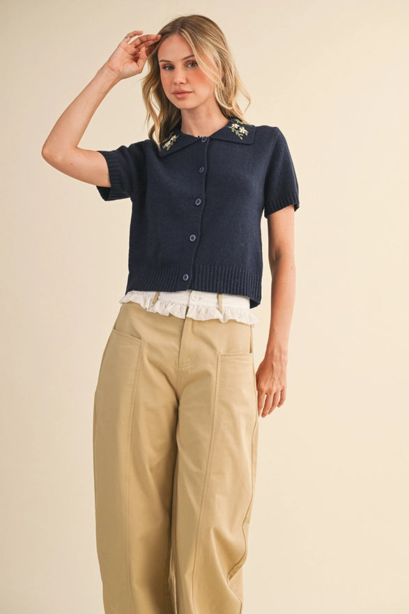 Woman wearing a navy cardigan, white blouse, and beige pants on a beige background