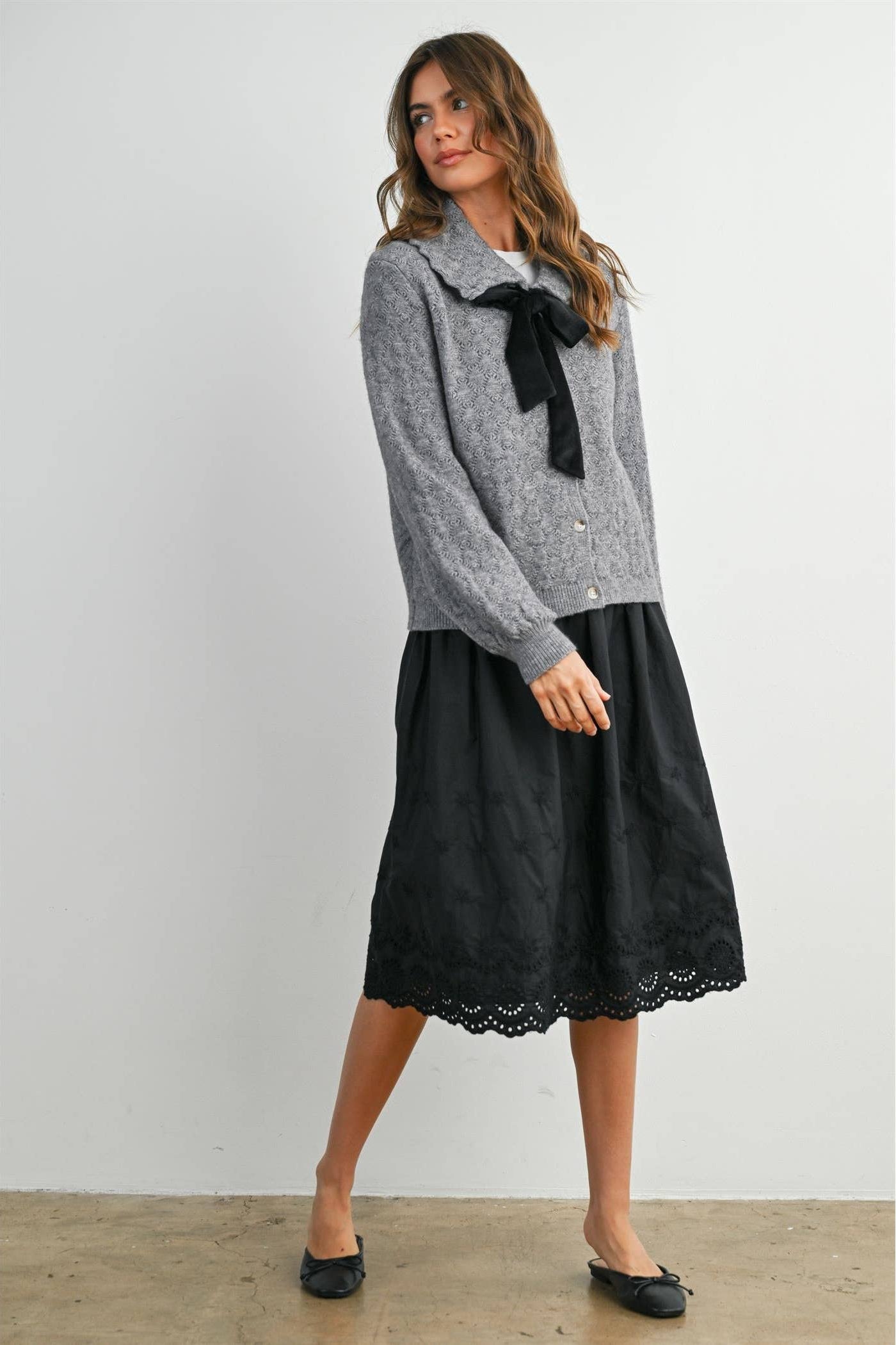 Woman wearing a gray sweater with a black bow and a black lace skirt against a white background