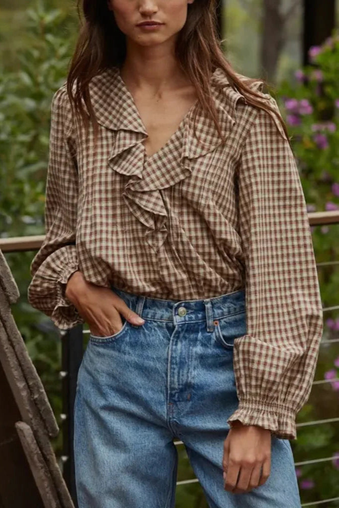 Woman wearing a checkered blouse and blue jeans with a blurred natural background