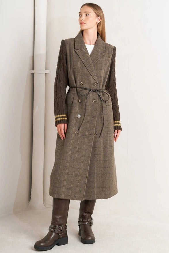 Woman wearing a long brown plaid coat with a belt on a white background
