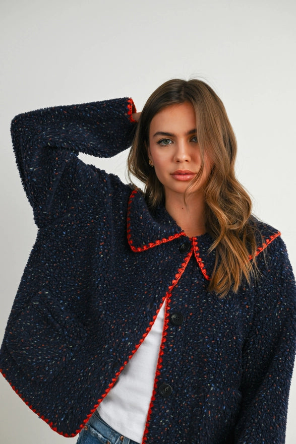 Woman wearing a dark blue textured jacket with red trim on a white background