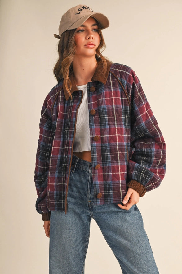 Woman wearing a plaid shirt, white top, and jeans with a beige cap on a neutral background